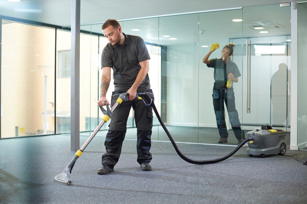 A worker cleans a carpeted office space with a commercial vacuum cleaner, showcasing a tidy, modern environment.